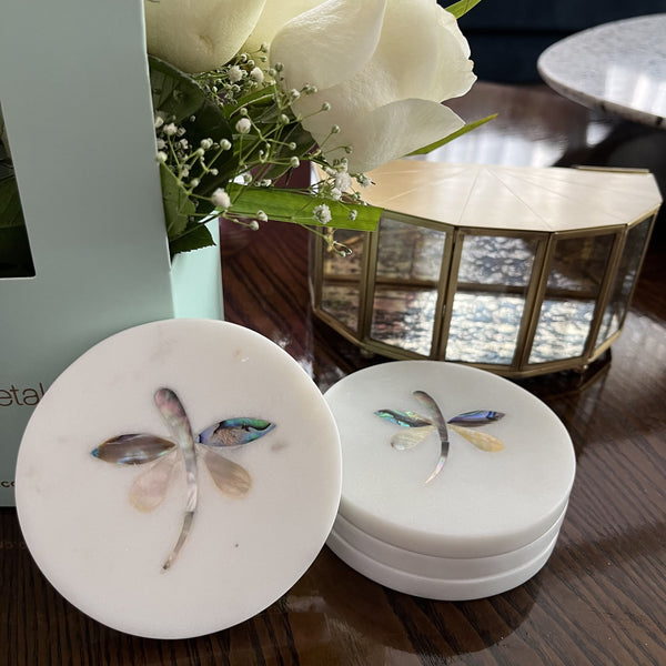 The image shows elegant dragonfly coasters made from white marble, featuring inlaid mother-of-pearl accents. These handmade coasters add a touch of luxury and style to any setting.